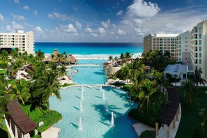 Un resort con piscina central, palmeras y vista a la playa.