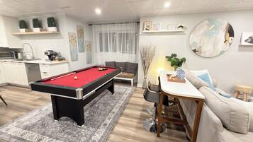 Una sala de estar moderna con mesa de billar, sofá, mesa de comedor y zona de cocina.