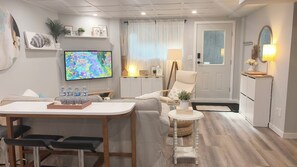 A modern living room with a sofa, a coffee table, a TV, and a dining area with chairs and a table. - IRISÉA Guest Suite with Private Entrance (Surrey)