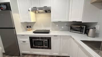A modern kitchen with white cabinetry, a built-in oven, a microwave, a toaster, and a kettle.