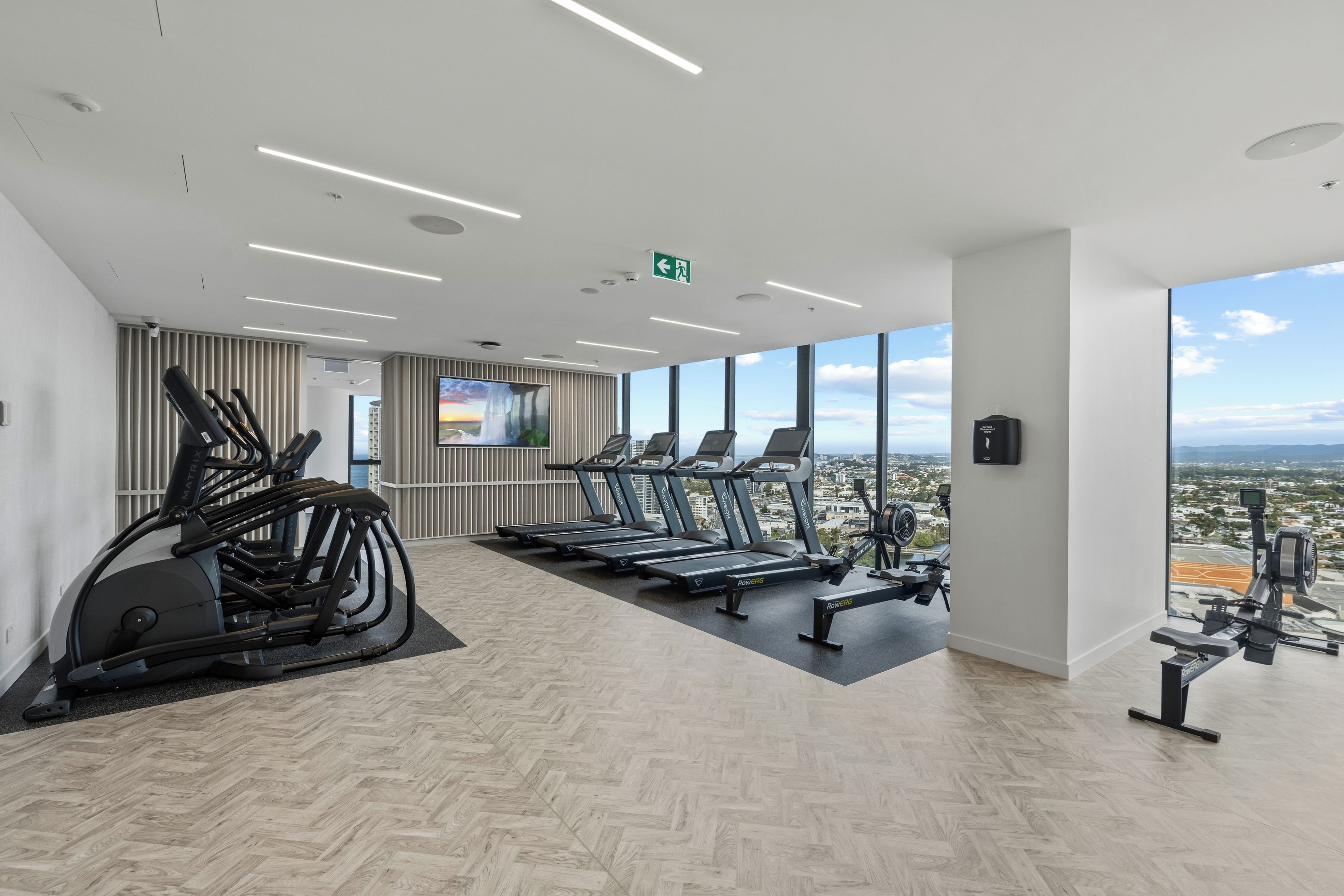 Ein modernes Fitnessstudio mit Trainingsgeräten, einem großen Fernsehbildschirm und Blick auf die Stadt.