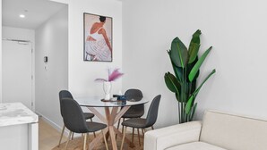Una zona menjador moderna amb taula de vidre, quatre cadires grises, un sofà blanc, una planta verda gran i una obra d'art emmarcada a la paret.