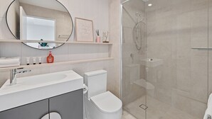 Un bany modern amb dutxa de vidre, un lavabo blanc i un vàter.