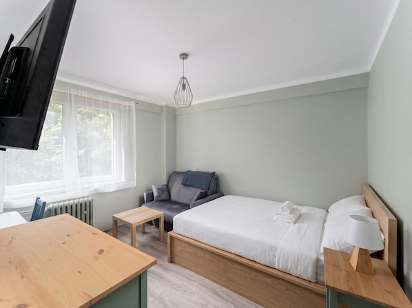 Ein Schlafzimmer mit Bett, Stuhl, Schreibtisch und Fernseher.