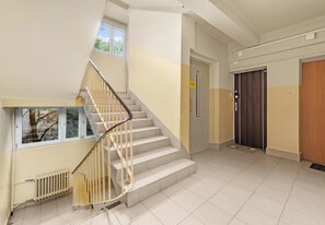 A staircase with a handrail leading to an upper floor, a door with a sign, and a radiator on the wall. - Kazimierza Wielkiego Charming Studio (Kraków)