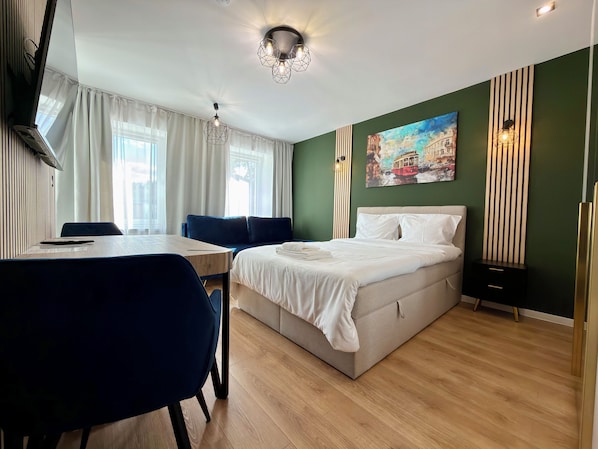 A hotel room with a bed, a desk, a chair, and a painting on the wall. - Oleśnicka Deluxe Studio (Wrocław)