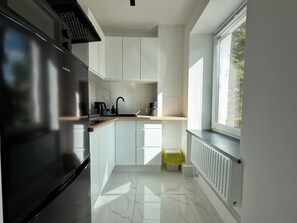 A modern kitchen with white cabinets, a black refrigerator, a sink, and a window providing natural light. - Oleśnicka Deluxe Studio (Wrocław)