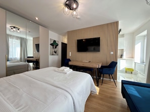 A modern hotel room with a large bed, a desk, a chair, a flat-screen TV mounted on a wooden panel wall, and a large mirror. - Oleśnicka Deluxe Studio (Wrocław)