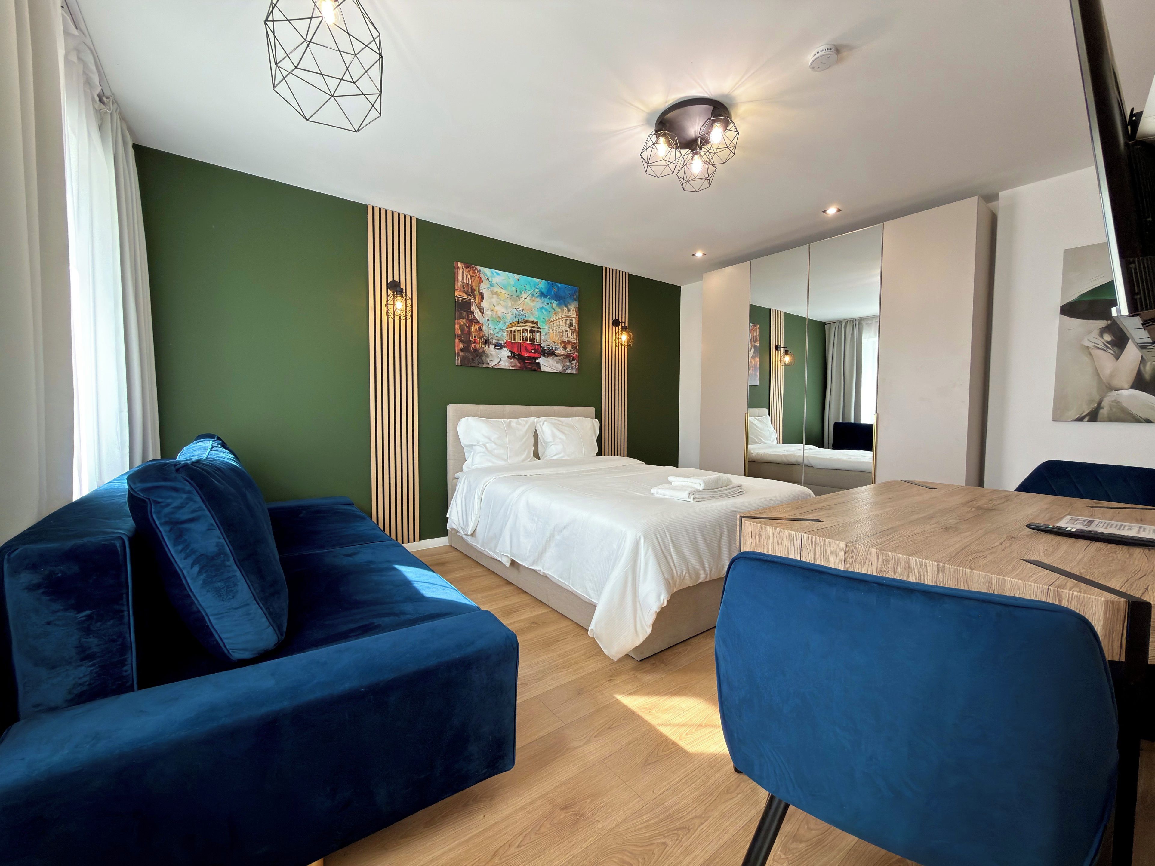 Un hotel modern amb un llit, un sofà blau, una taula de dinar de fusta i un quadre a la paret.