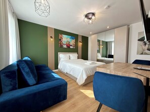 A modern hotel room with a bed, a blue sofa, a wooden dining table, and a large mirror. - Oleśnicka Deluxe Studio (Wrocław)
