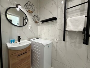 A modern bathroom with a white sink, a mirror, a towel rack, and a built-in washing machine. - Oleśnicka Deluxe Studio (Wrocław)