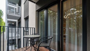 A balcony with a table and chairs, a view through a glass door, and a railing. - Manufaktura Signature Studio (Łódź)