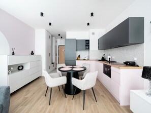 A modern kitchen with a round dining table, white chairs, grey cabinets, and a black countertop. - Manufaktura Signature Studio (Łódź)