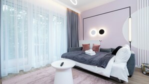 A modern bedroom with a large bed, a bedside table, a round mirror, and a wall-mounted light fixture. - Manufaktura Signature Studio (Łódź)