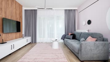 A modern living room with a flat-screen TV, grey sofa, white side table, and a pink rug.