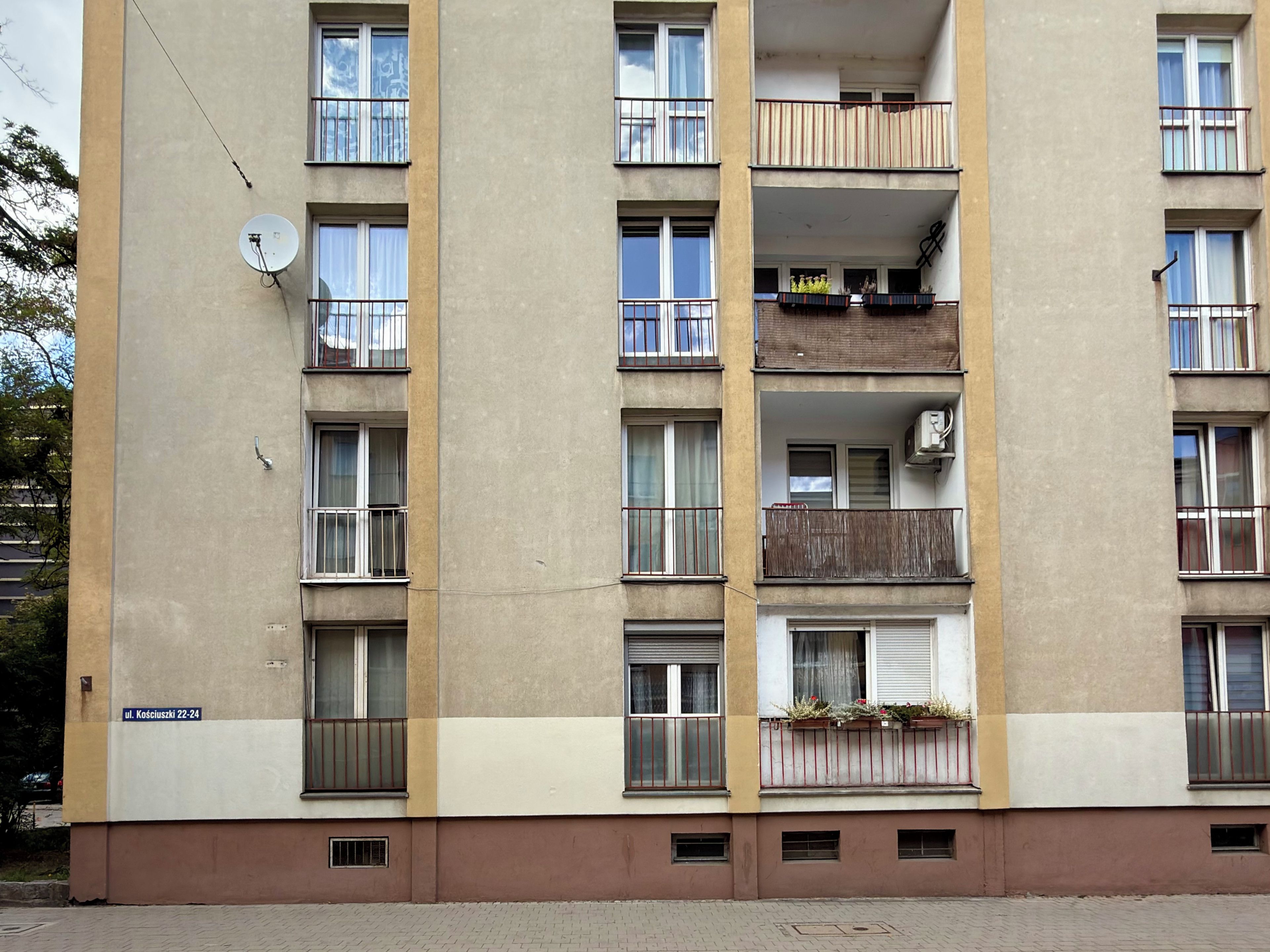 Un edificio residencial de varios pisos con balcones, antena parabólica y un letrero de dirección visible.