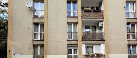 Un edificio residencial de varios pisos con balcones, antena parabólica y un letrero de dirección visible.
