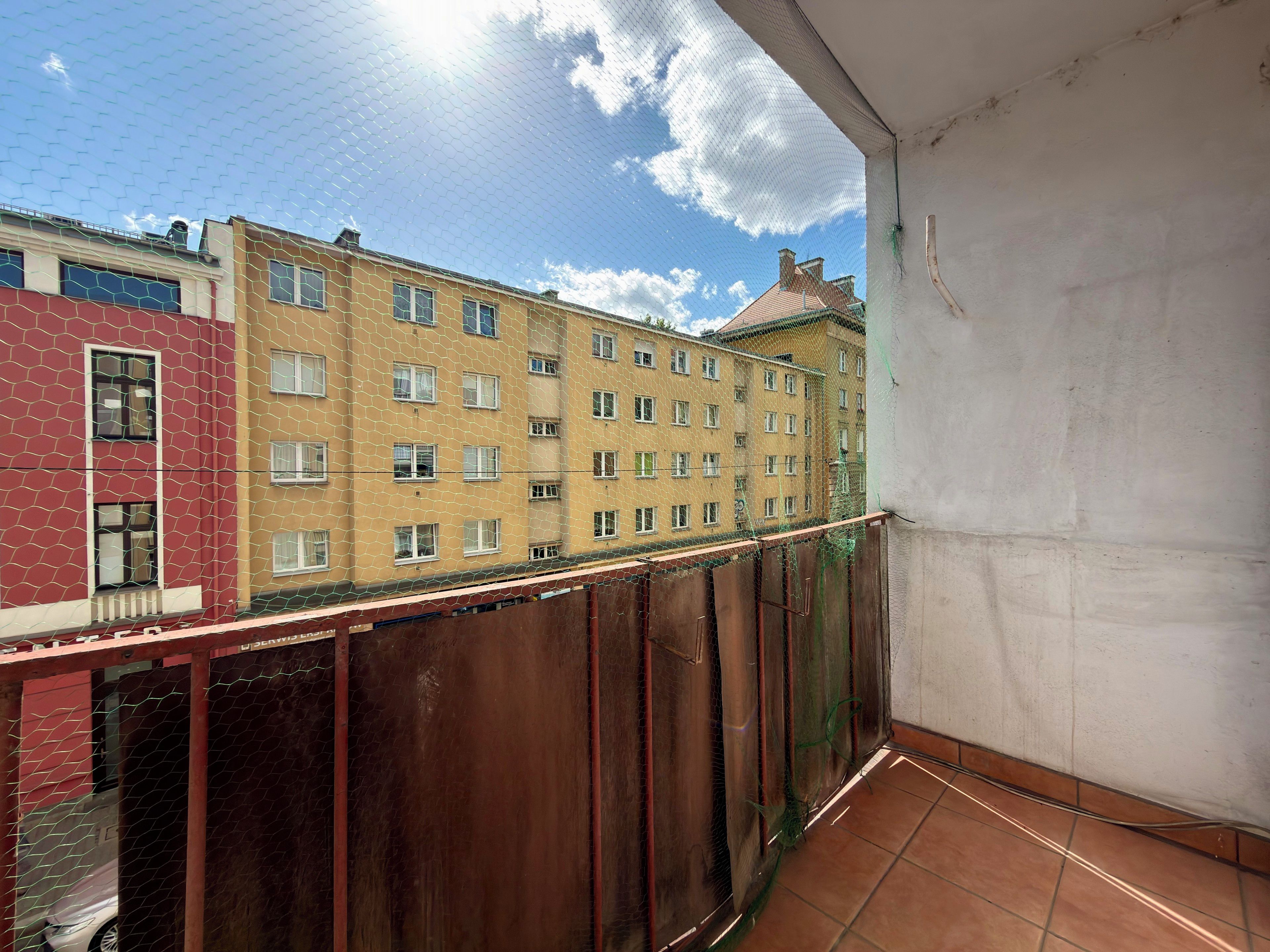 En balkong med utsikt över en gul byggnad med många fönster och en röd byggnad i bakgrunden.