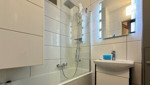 Ein modernes Badezimmer mit einer gläsernen Duschkabine, einer weißen Badewanne und einem Waschbecken mit Spiegel darüber.
