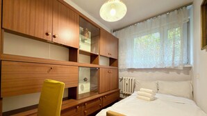 Ein Schlafzimmer mit einem Bett, einem Holzschrank, einem Sessel und einem Fenster mit Vorhängen.