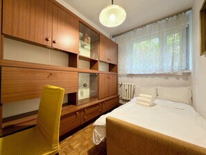 A bedroom with a bed, a wooden wardrobe, a chair, and a window with curtains. - Kościuszki Central Apartment #7 (Wrocław)