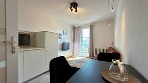 Una stanza moderna con un tavolo da pranzo, sedie, televisione e una porta scorrevole in vetro che dà su un balcone.