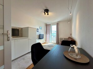 Ein modernes Zimmer mit Esstisch, Stühlen, einem Fernseher und einer Glastür zum Balkon.