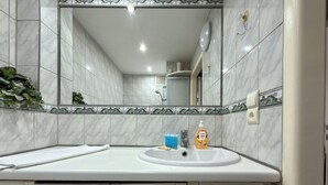 Un bagno con lavandino bianco, specchio e pareti piastrellate.