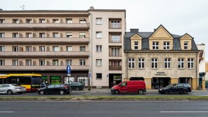 A multi-story building with a flat facade, a bus stop, and parked cars on the street. - Kopcińskiego Cozy City Studio (Łódź)