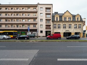 En flereetagers bygning med en flad facade, en busholdeplads og parkerede biler på gaden.