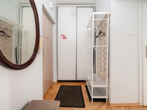 Habitació d'hotel amb terra de fusta, una porta blanca amb un senyal vermell, un mirall, una catifa negra i un moble prestatge metàl·lic blanc.