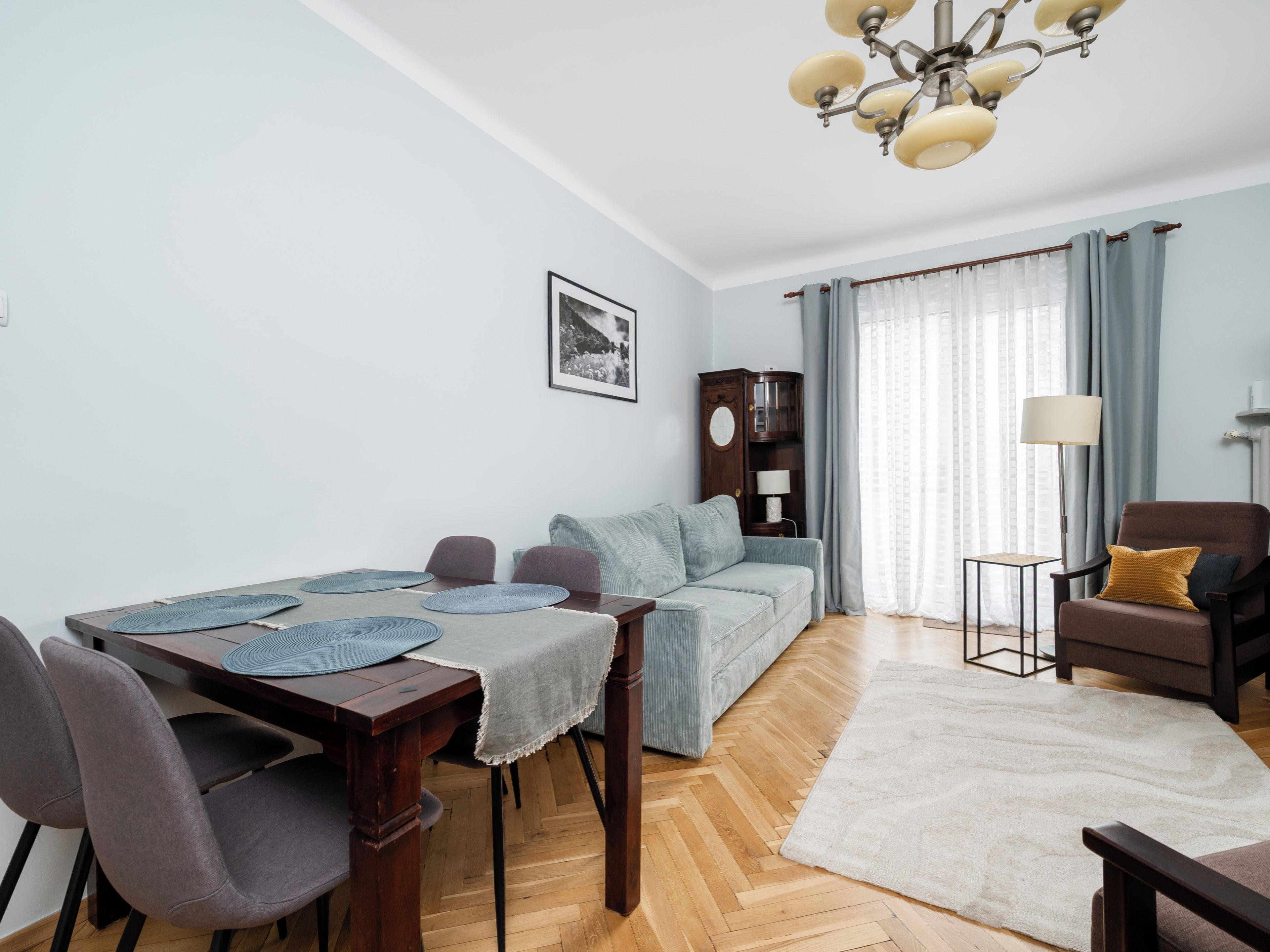 Ein Wohnzimmer mit Esstisch, Sofa, Sesseln und einer Lampe.