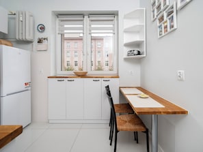 Une cuisine moderne avec des armoires blanches, un plan de travail en bois, un four encastré et une fenêtre donnant sur des immeubles.