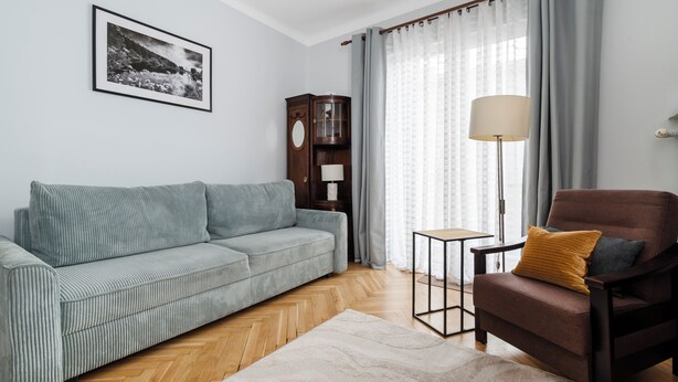 A living room with a sofa, a chair, a lamp, a cabinet, and a framed picture on the wall. - Kopcińskiego Cozy City Studio (Łódź)