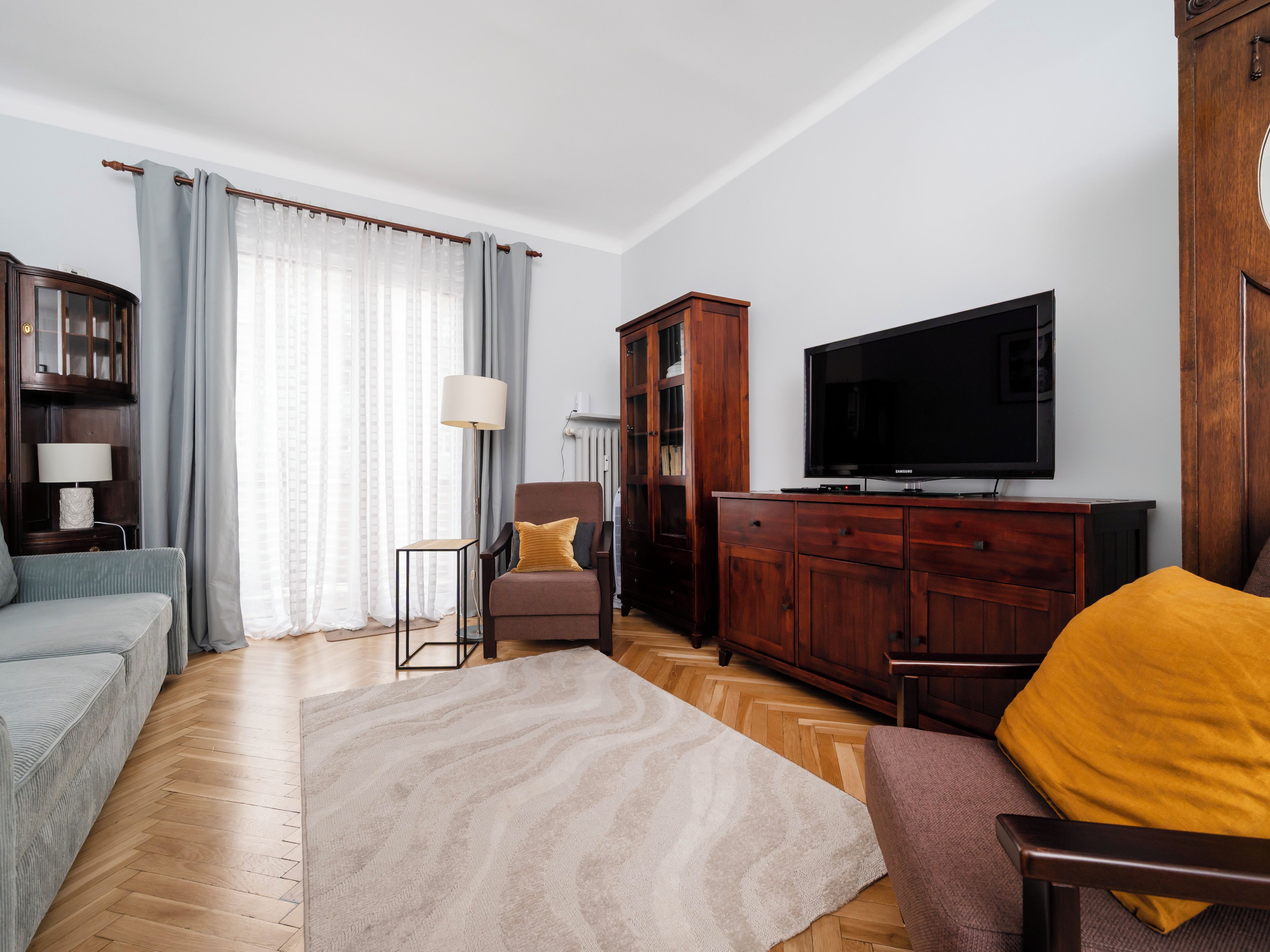 Ein Wohnzimmer mit einer Couch, einem Sessel, einem Holzschrank, einem Fernseher und einer Lampe.
