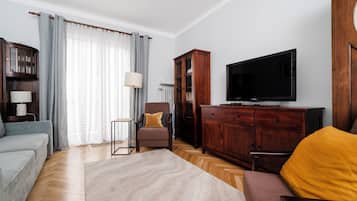 Ein Wohnzimmer mit einer Couch, einem Sessel, einem Holzschrank, einem Fernseher und einer Lampe.