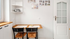 A small kitchen with a wooden table, two chairs, a white door, and a shelf with a radio. - Kopcińskiego Cozy City Studio (Łódź)