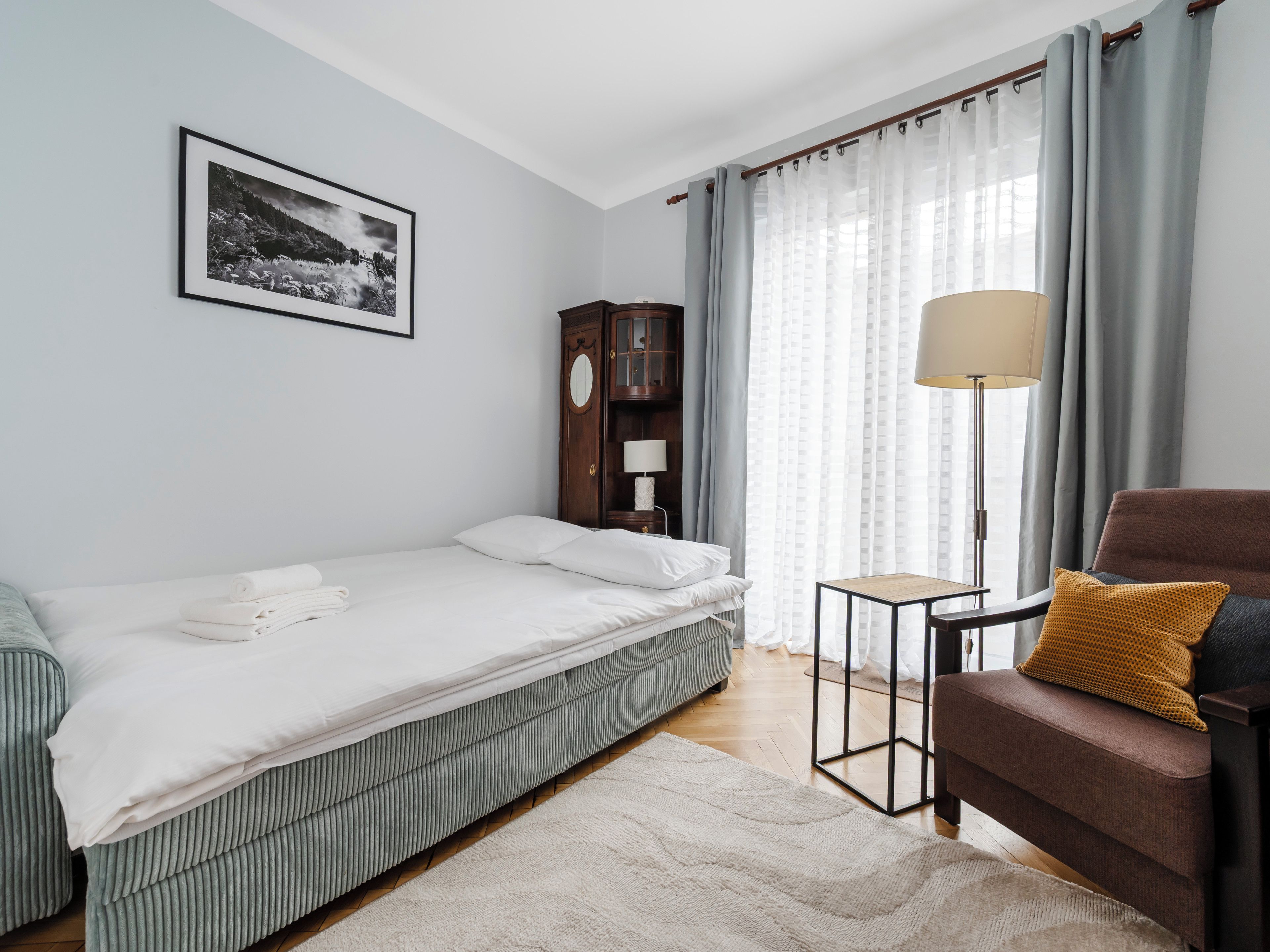 Ein Schlafzimmer mit einem Bett, einem Sessel, einer Lampe, einem Kleiderschrank und einem gerahmten Bild an der Wand.