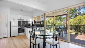 A modern kitchen with a dining area, a refrigerator, an oven, and a clock on the wall.