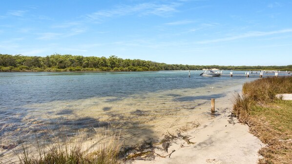 A clear water body with a sandy shore, a boat dock, and a forested area in the background.