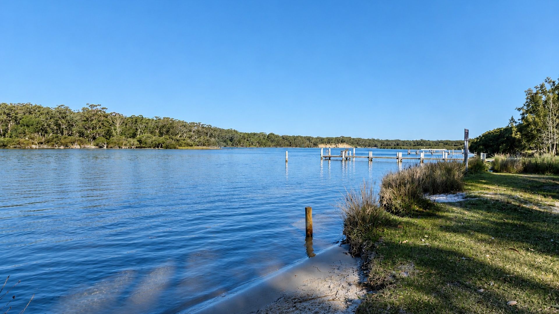 Un lac paisible avec une jetée qui s’avance sur l’eau, entouré de prairies et d’arbres.
