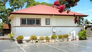 A two-story building with a red roof, white siding, and a small front porch with potted plants.