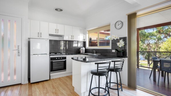 A modern kitchen with white cabinets, a black countertop, and a built-in oven. There is a window with a view of trees and a clock on the wall.