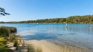 A clear lake with a sandy beach and dense trees in the background.