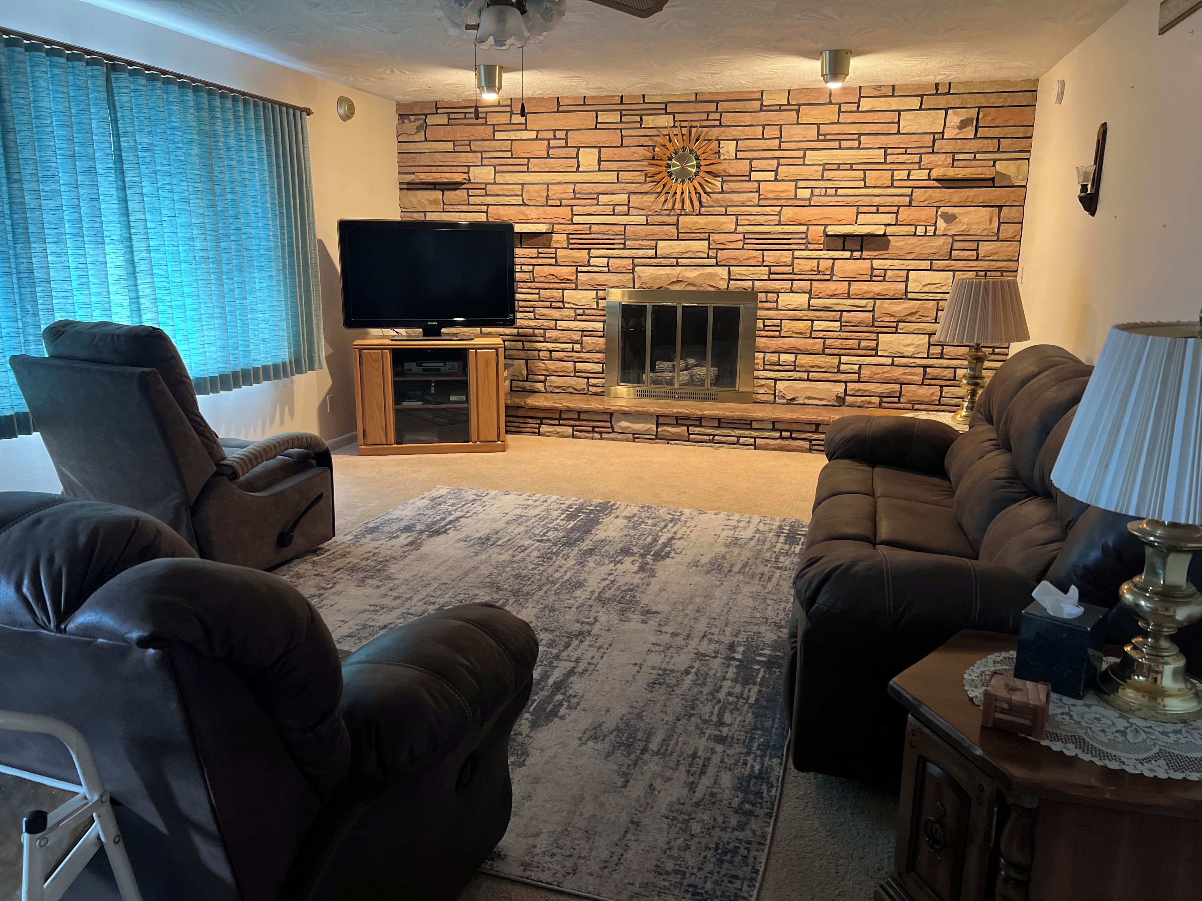 A living room with a stone wall, a fireplace, a television, and two sofas.