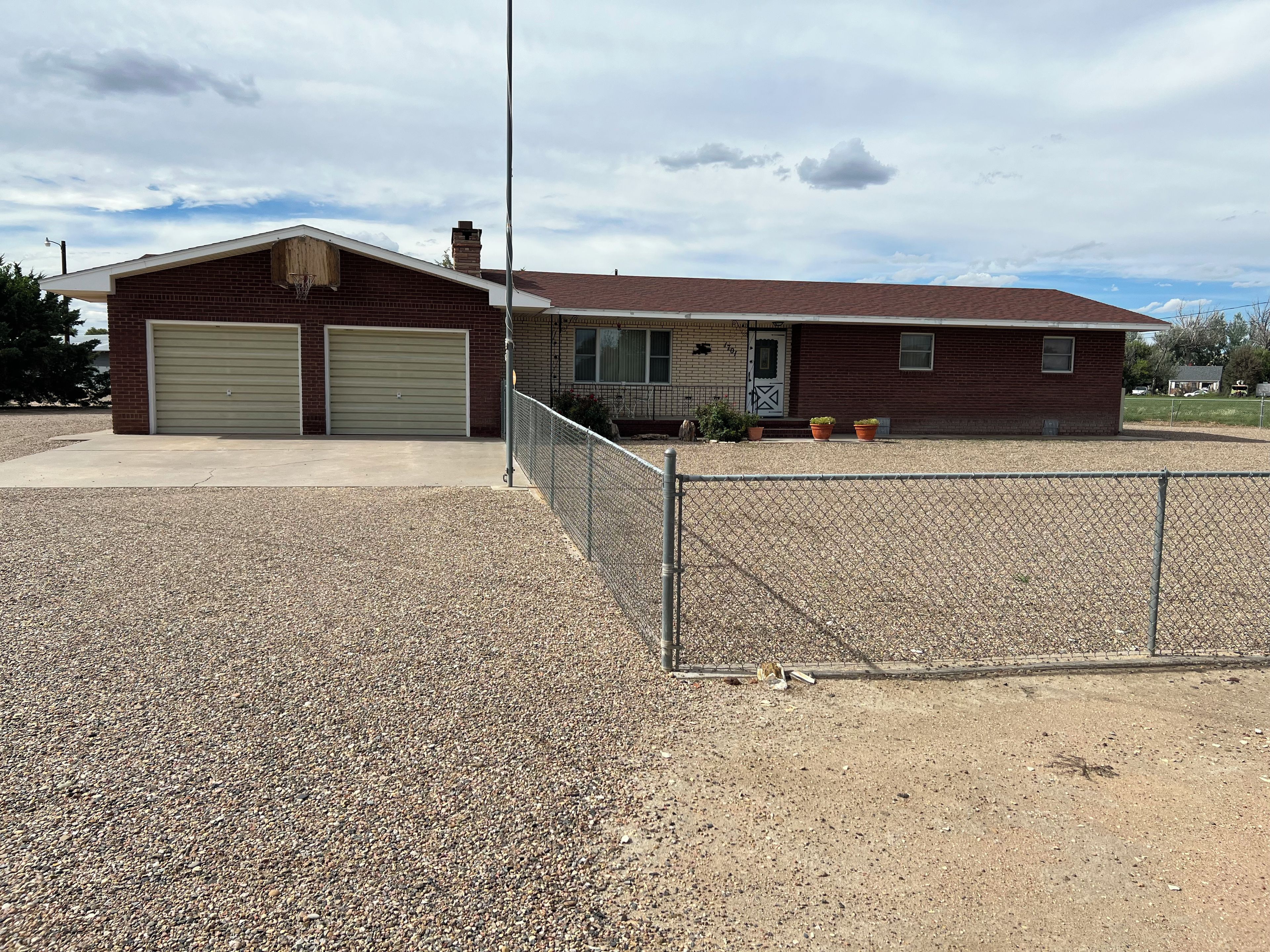 A single-story building with two garage doors, a fenced driveway, and a clear sky.