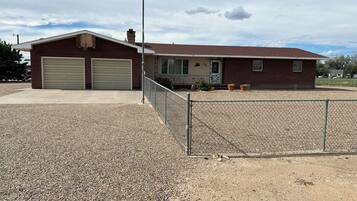 A single-story building with two garage doors, a fenced driveway, and a clear sky.