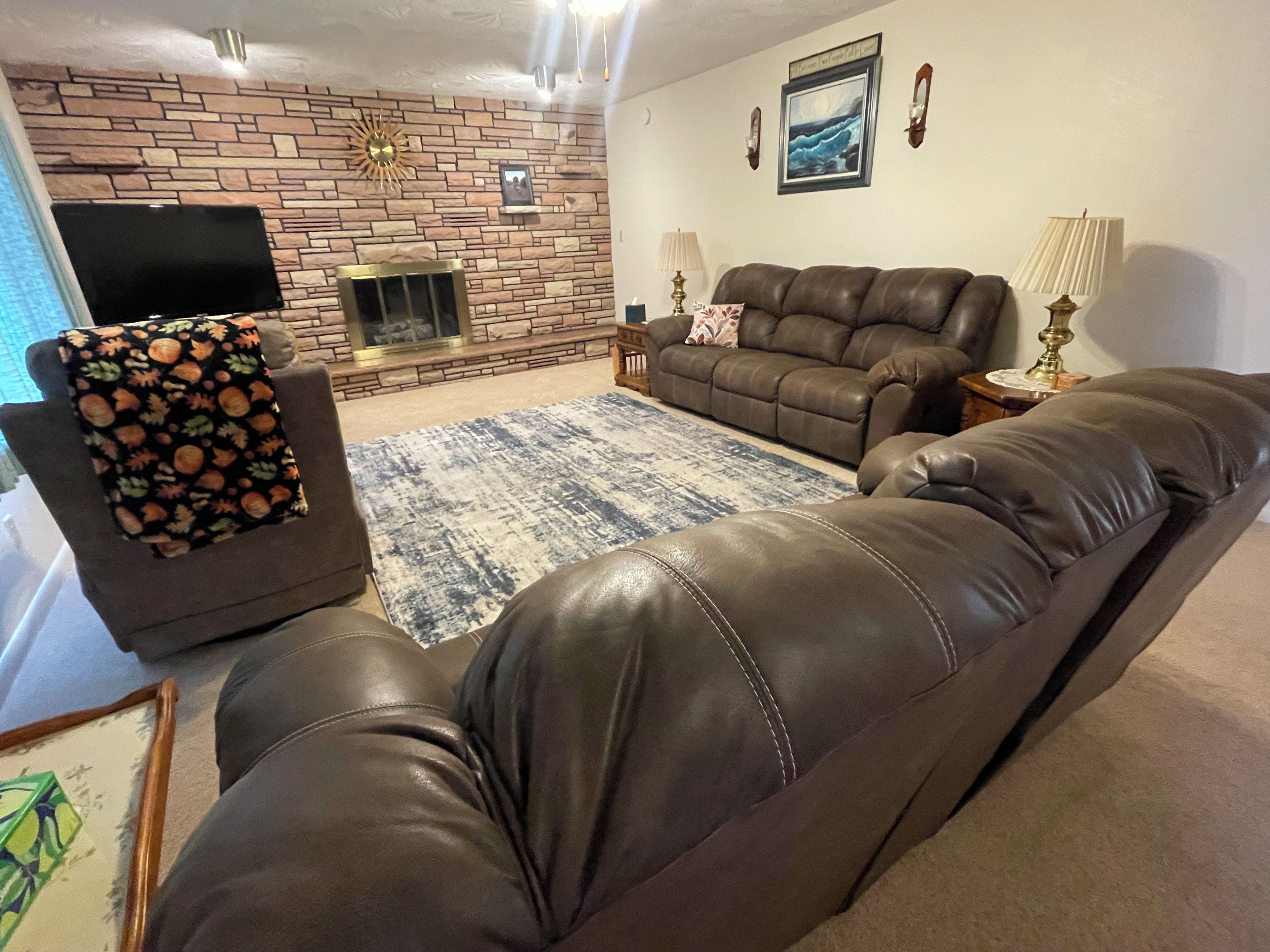 A living room with a leather sofa, a fireplace, a television, and a patterned throw on a chair.