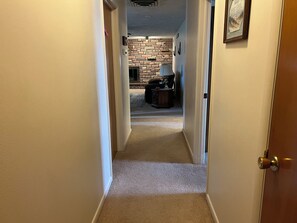 A carpeted hallway leading to a room with a brick wall and a fireplace.