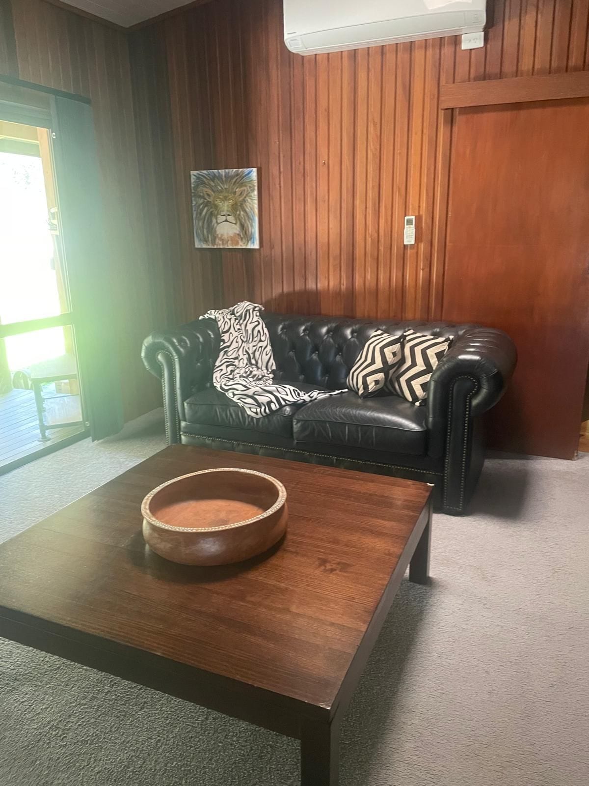 A room with a leather sofa, a wooden coffee table, and a painting on the wall.